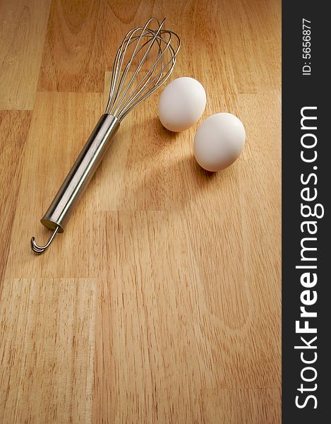 Whisk and Eggs on a wooden background.