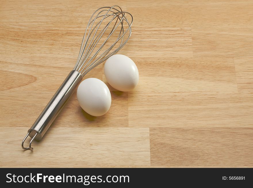 Whisk and Eggs on a wooden background.