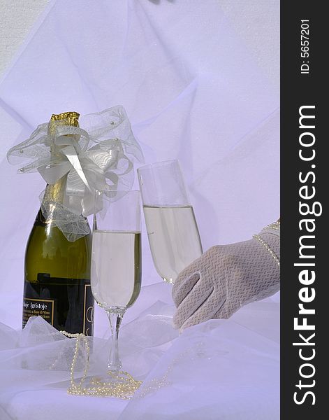 Bottle of champagne, two glasses, bride's hand in wedding glove, holding one of them. Bottle of champagne, two glasses, bride's hand in wedding glove, holding one of them