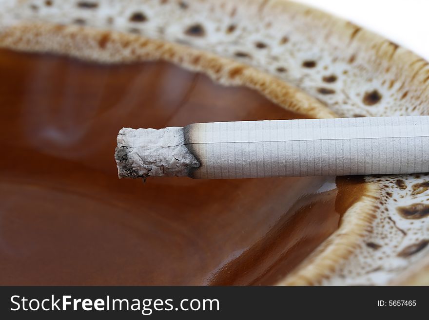 Cigarette in brown ceramic ash-tray on white background. Cigarette in brown ceramic ash-tray on white background
