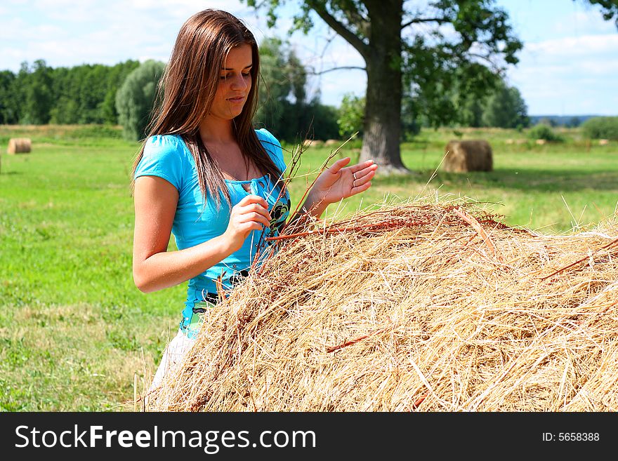 Young woman on the meadow in the summer behind a big bale of hay. Young woman on the meadow in the summer behind a big bale of hay