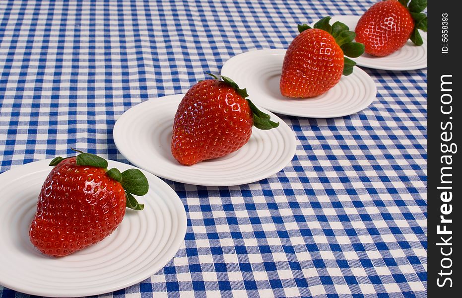 Delicious fresh strawberries served on individual plates on a blue gingham tablecloth. Delicious fresh strawberries served on individual plates on a blue gingham tablecloth