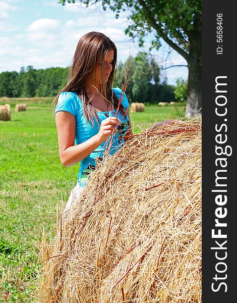 Young woman on the meadow in the summer behind a big bale of hay. Young woman on the meadow in the summer behind a big bale of hay