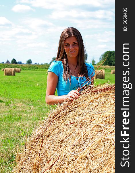 Young woman on the meadow in the summer behind a big bale of hay. Young woman on the meadow in the summer behind a big bale of hay