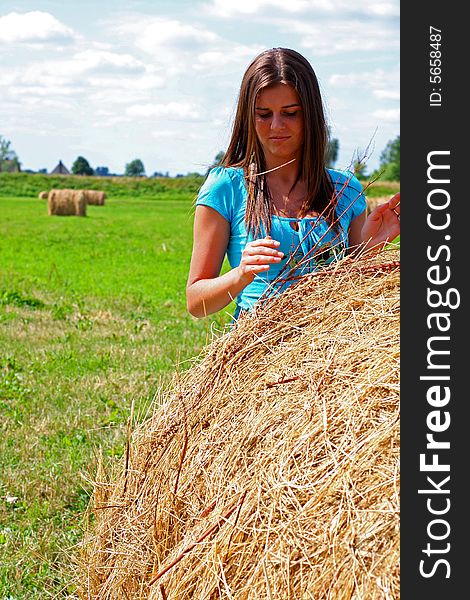 Young woman on the meadow in the summer behind a big bale of hay. Young woman on the meadow in the summer behind a big bale of hay