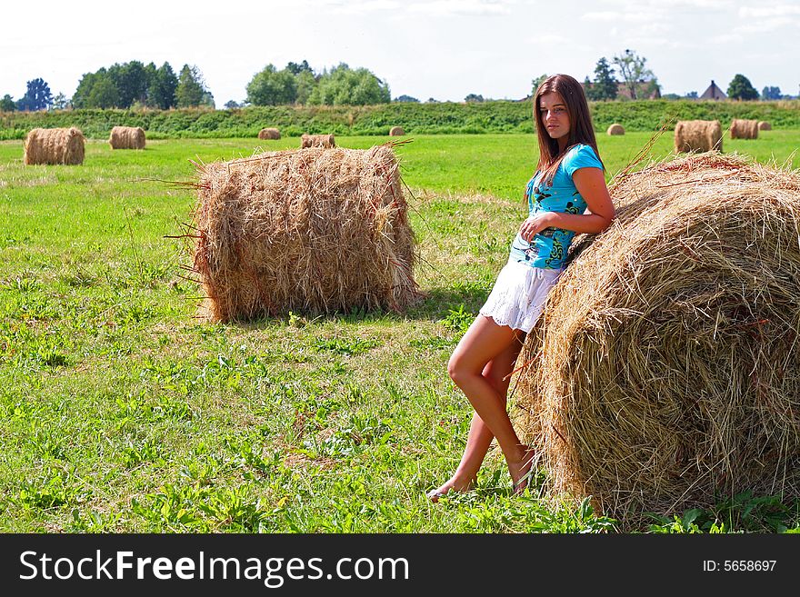 Young woman on the meadow in the summer behind a big bale of hay. Young woman on the meadow in the summer behind a big bale of hay