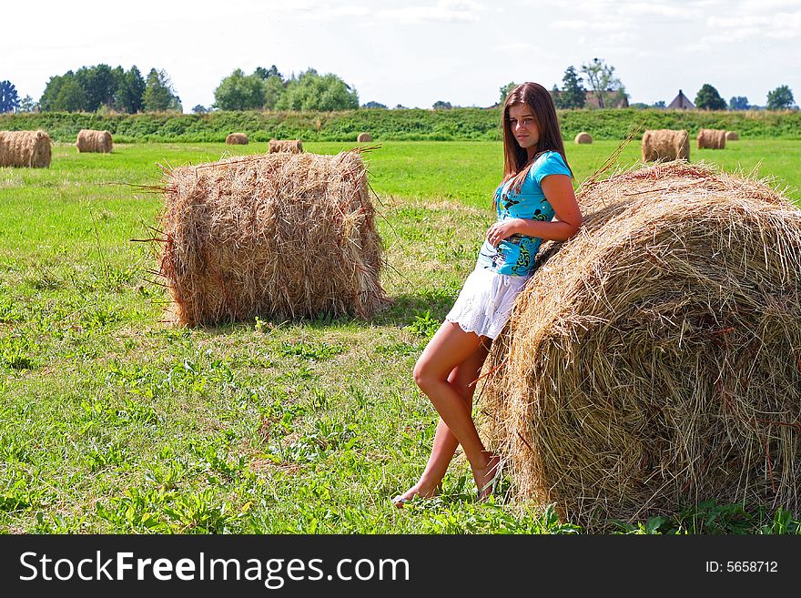 Young woman on the meadow in the summer behind a big bale of hay. Young woman on the meadow in the summer behind a big bale of hay