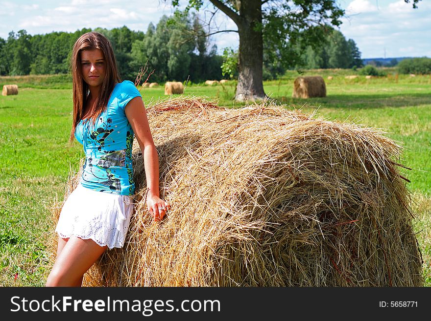 Young woman on the meadow in the summer behind a big bale of hay. Young woman on the meadow in the summer behind a big bale of hay