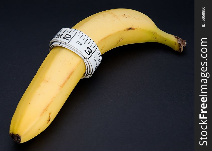 A banana with a tape measure wrapped around it isolated on a black background. A banana with a tape measure wrapped around it isolated on a black background.