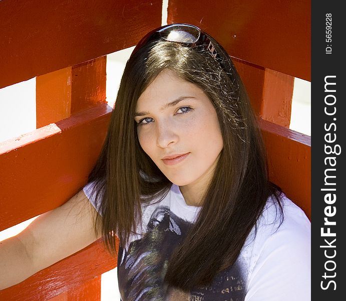 Young woman leaning against a red fence looking at the camera. Young woman leaning against a red fence looking at the camera.