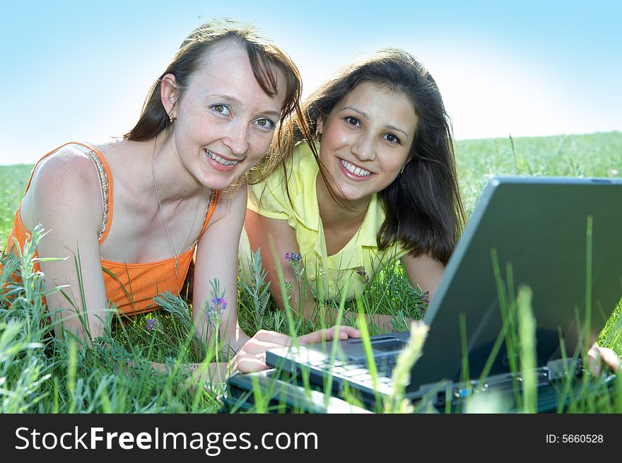 Two beautiful girls with laptop computer on green grass