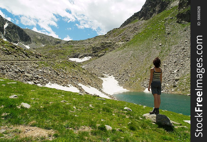 A girl staring at the beautiful mountain landscape with a lake, grass and snow. This picture is from Alps, in Italy. A girl staring at the beautiful mountain landscape with a lake, grass and snow. This picture is from Alps, in Italy.