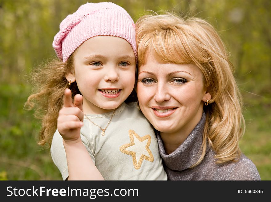 Small blond girl in a pink cap with mum shows a finger outdoors. Small blond girl in a pink cap with mum shows a finger outdoors