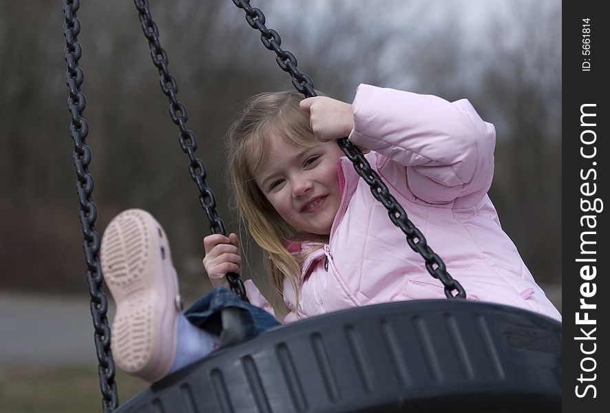 Happy 4 year old blond girl swinging on tire swing, outdoors