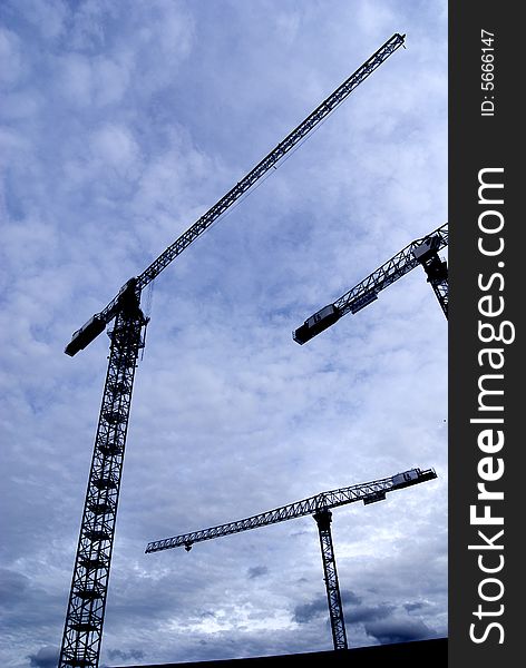 Three construction cranes silhouette midday