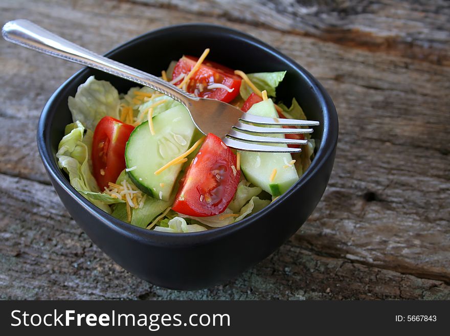 Fresh house salad in a black bowl with a fork.  All done on an old wood textured background.  Copy space also available.