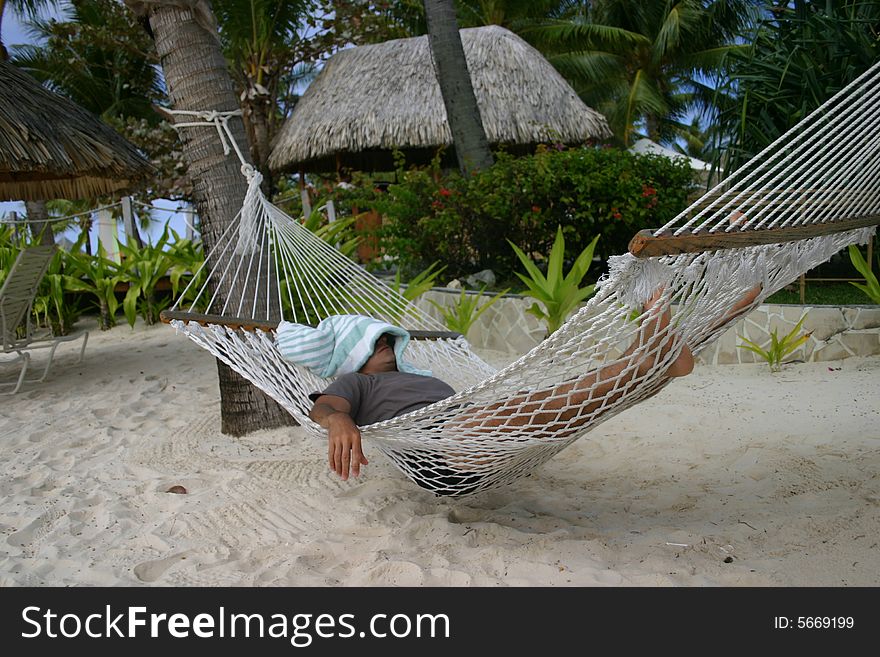 A man sleeping on the beach in a hammock.