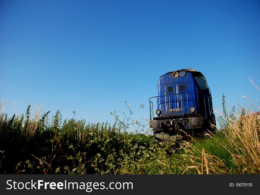 Blue train approaching between green field and blue sky