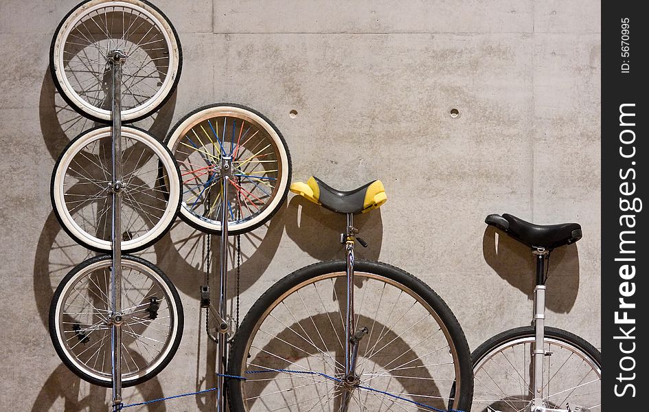 A variety of unicycles leaning against a cement wall