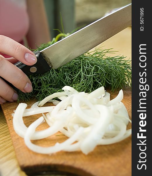 Female hand holding knife above board with dill and onion. Female hand holding knife above board with dill and onion