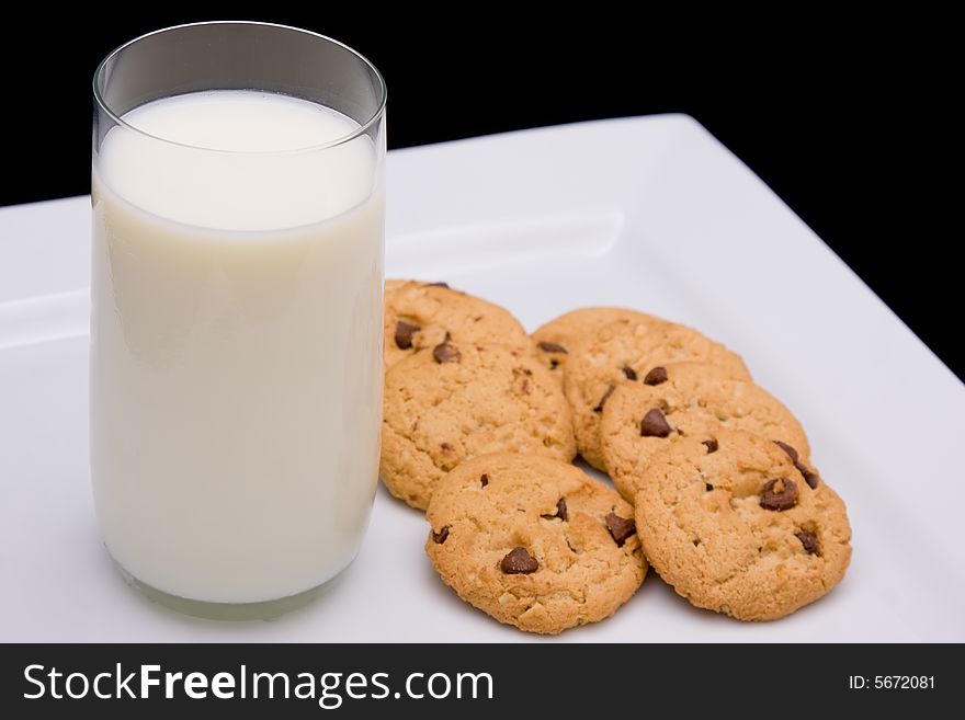A glass of milk and half a dozen cookies on a plate against a black background. A glass of milk and half a dozen cookies on a plate against a black background