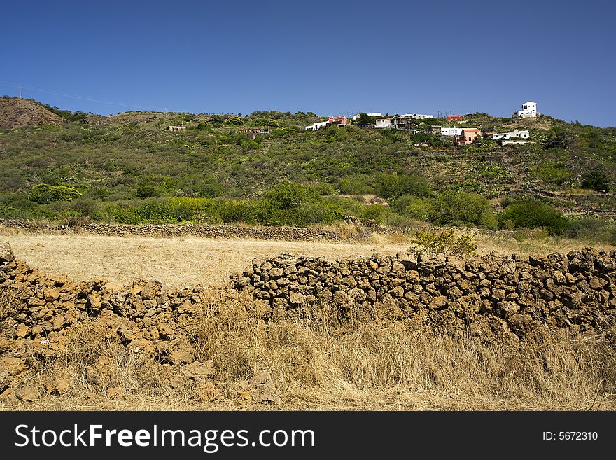 Small village in the mountains at eastern coast of the canary island of El Hierro, crumbling lavastone wall in foreground. Small village in the mountains at eastern coast of the canary island of El Hierro, crumbling lavastone wall in foreground