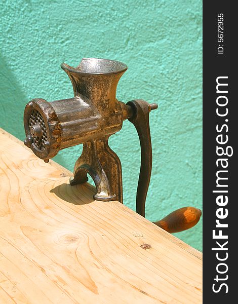 Antique meat grinder on weathered wooden table against turquoise wall