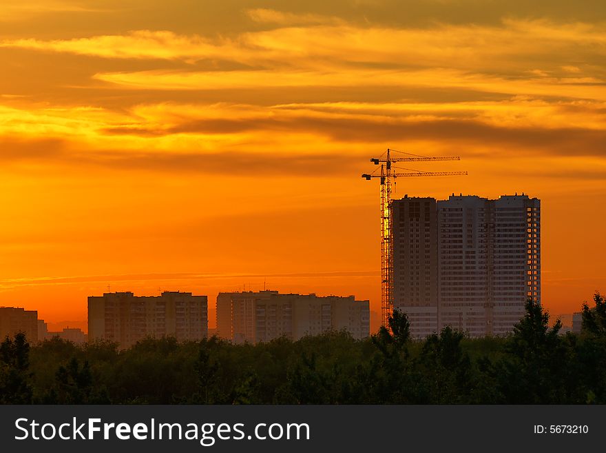 Construction of a building, cranes and other machinery as silhouettes against a background of red sunset sky. Construction of a building, cranes and other machinery as silhouettes against a background of red sunset sky