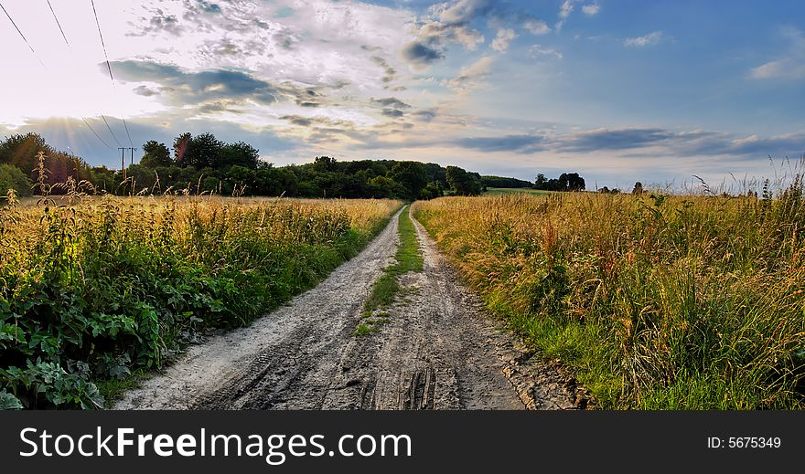 Field earth road in time sunset with cloudy sky. Field earth road in time sunset with cloudy sky