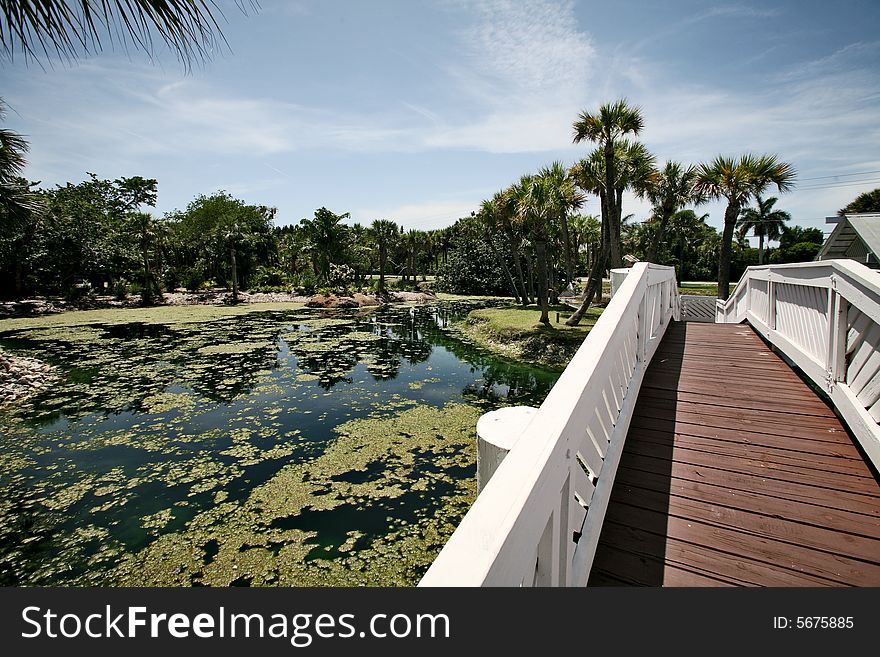 A photo of a white bridge crossing over a man made pond. A photo of a white bridge crossing over a man made pond.