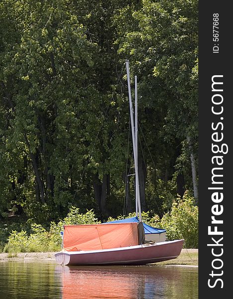 A small orange sail boat near the shore