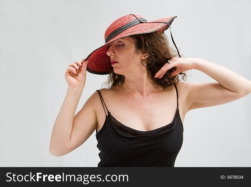 Serene middle aged woman wearing a red hat tipping it over with 1 hand, isolated. Serene middle aged woman wearing a red hat tipping it over with 1 hand, isolated