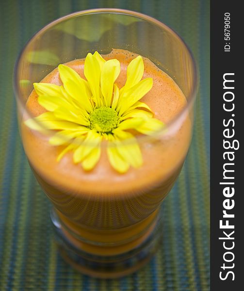 A daisy bathes inside of a glass of freshly juiced raw produce, on a striped table setting. A daisy bathes inside of a glass of freshly juiced raw produce, on a striped table setting.