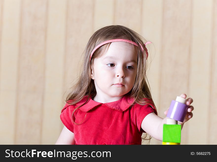 Portrait of a little girl building toy tower from wooden bricks at home