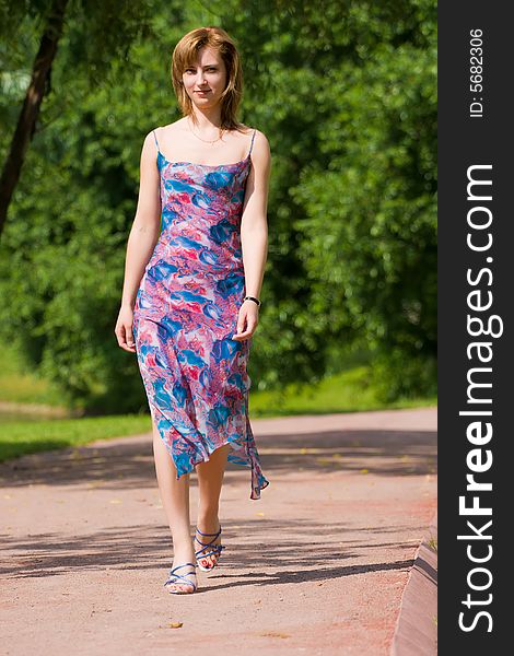 Beautiful young girl in a summer dress goes on a path in park. Beautiful young girl in a summer dress goes on a path in park