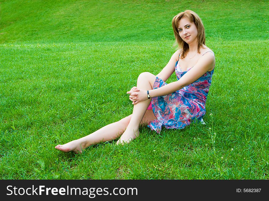 Young attractive girl sits on a green grass. Young attractive girl sits on a green grass