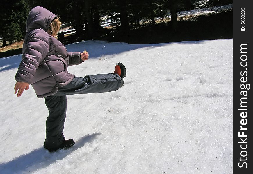 Child playing in the snow, kicking snow to make the snowflakes fly