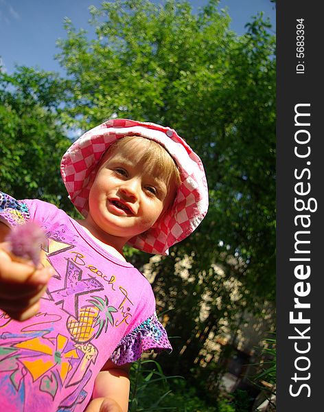 Little smiling girl with a flower against a tree