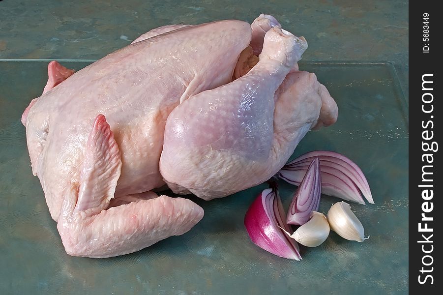 Whole fresh chicken on glass chopping board with spanish onion and garlic cloves. Whole fresh chicken on glass chopping board with spanish onion and garlic cloves