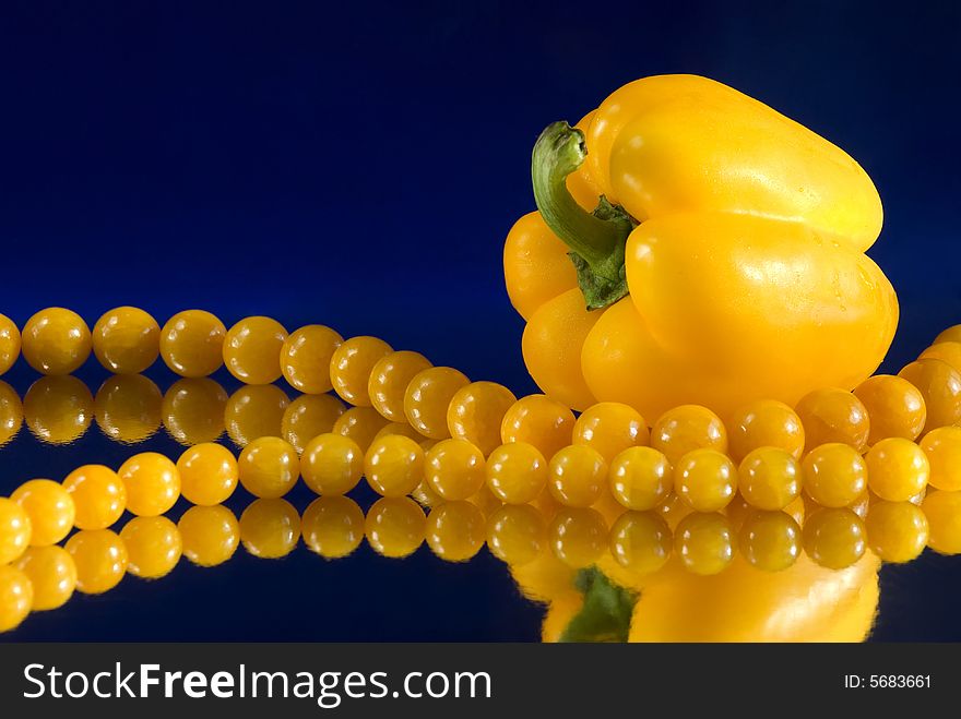 Yellow paprika and beads with reflection on blue background