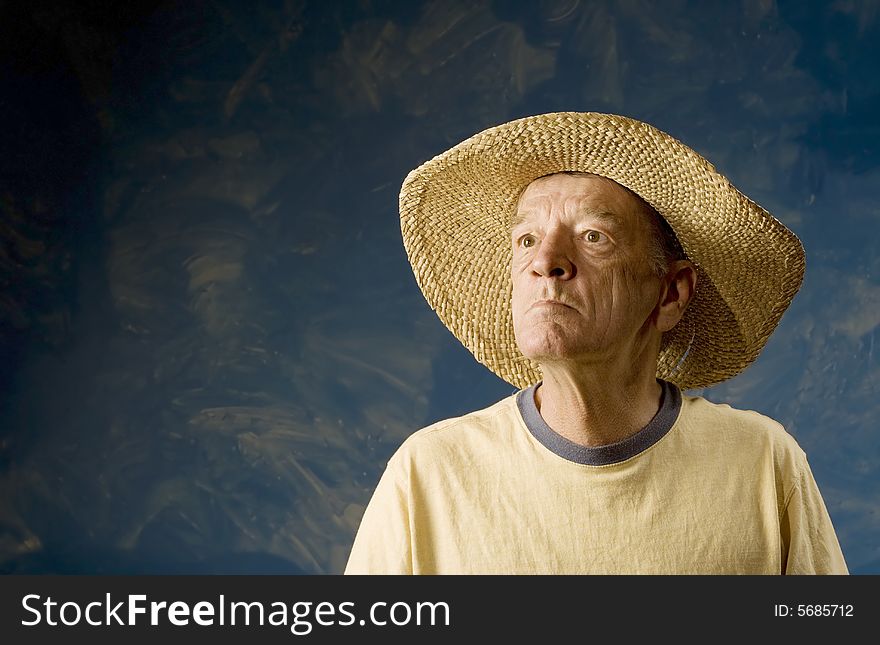 Senior man in a straw hat in front of blue set wall. Senior man in a straw hat in front of blue set wall