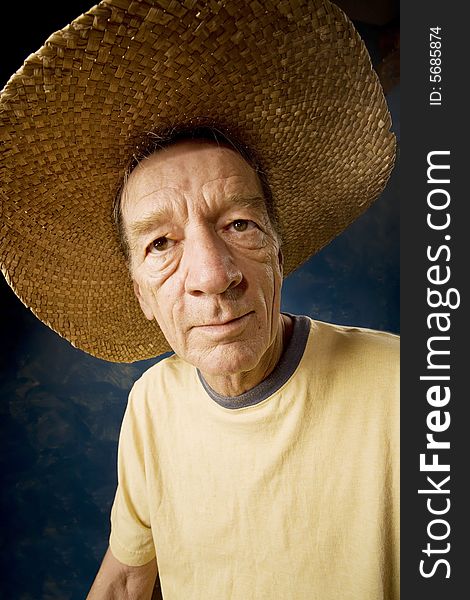 Senior man in a  big straw hat in front of blue set wall. Senior man in a  big straw hat in front of blue set wall