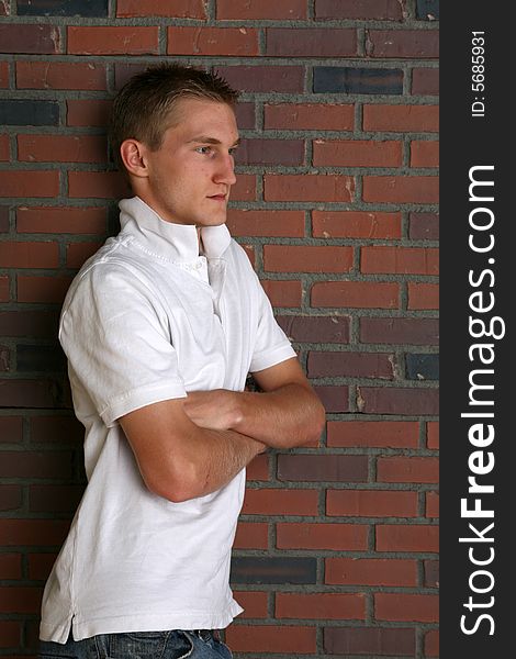 Buff and slim looking young man standing next to brick wall with arms crossed. Buff and slim looking young man standing next to brick wall with arms crossed