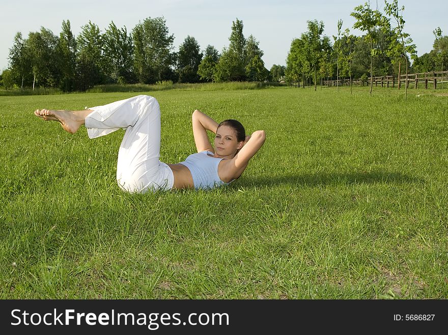 Sporty girl exercising on meadow against the sky.