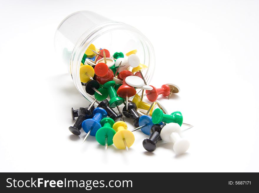 A plastic jar spilling colored thumb tacks. A plastic jar spilling colored thumb tacks.