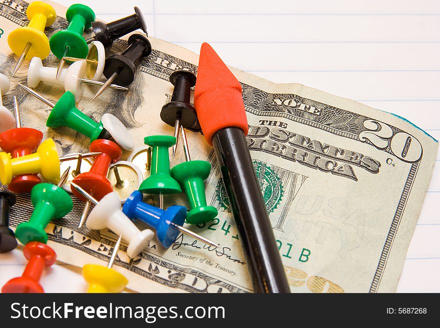 A twenty dollar bill with thumb tacks and a pencil representing buying back to school supplies.