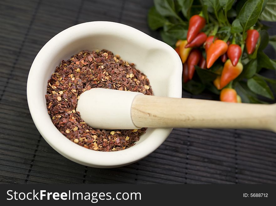 A pestle and mortar with crushed chilis and chili plant. A pestle and mortar with crushed chilis and chili plant