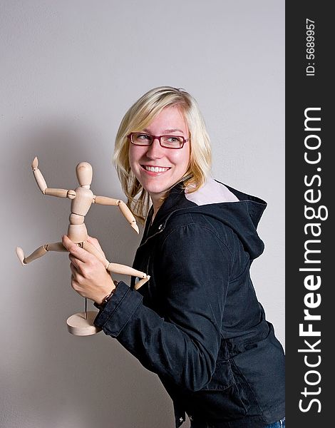 Young woman against a wall playing with a wooden doll in her hand who looks like its running. Young woman against a wall playing with a wooden doll in her hand who looks like its running.