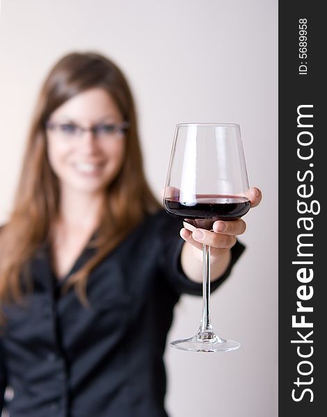 Modern young woman holding a wine glass with liquid in it doing a cheers motion. Focus in glass. Modern young woman holding a wine glass with liquid in it doing a cheers motion. Focus in glass.