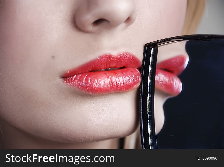 Scarlet lips are reflected in a little mirror which a girl holds in a hand